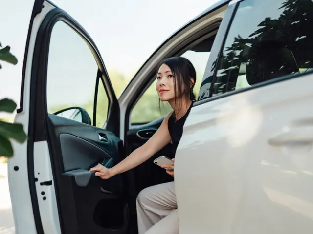 Jeune femme quittant le siège conducteur d’une minifourgonnette blanche.